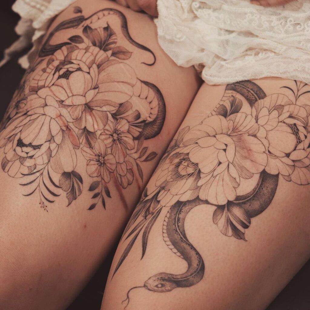 Scar cover up tattoos on a woman's thigh, covered by fine line peonies and a snake. 