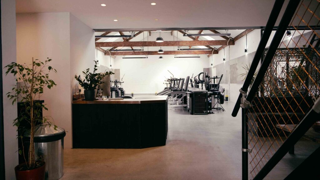 Image is of No Regrets Tattoo Studio in London. The studio is empty and shows a reception desk, waiting area, tattoo chairs and a mental stairs banister on the right of the image. 