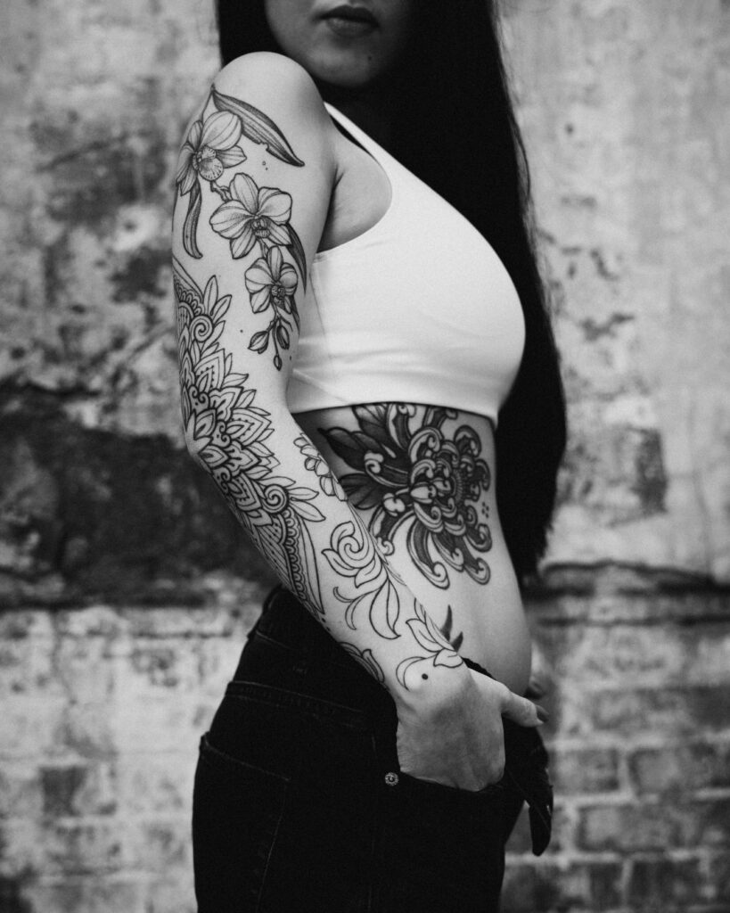 Kristina stands side on, her Chrysanthemum Tattoo is visible on her ribs as is her ornamental floral tattoo sleeve. 