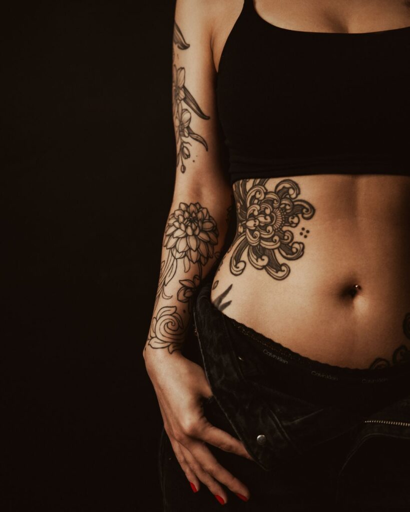 A close up on Kristina's torso shows her Chrysanthemum Tattoo  on her ribs and flowers on her forearm