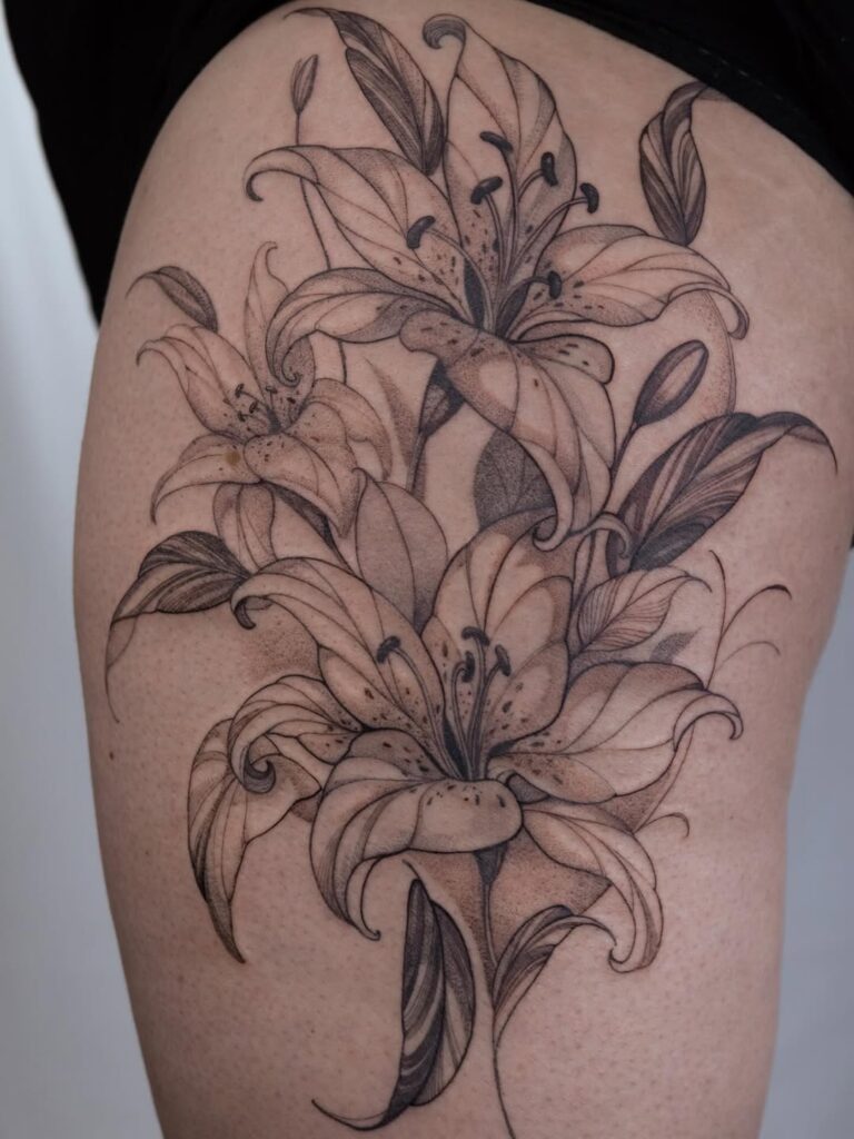 A fine line thigh tattoo of three lily's surrounded by leaves. Done by Robson Santos at No Regrets Bristol.