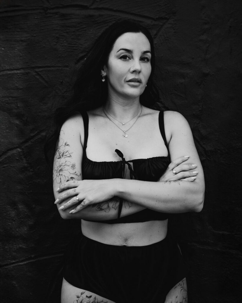 A Black and white image of Stacey standing face on to the camera with her arms crossed. 