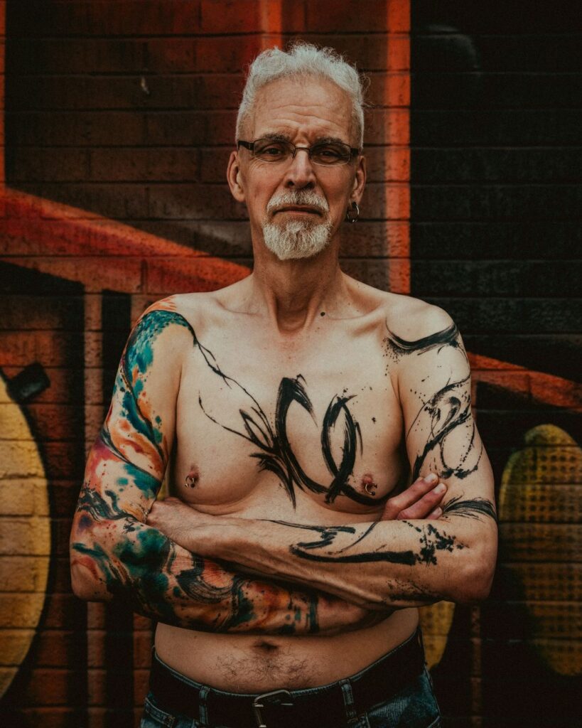 A man standing straight on to the camera with abstract paint stroke tattoos. 