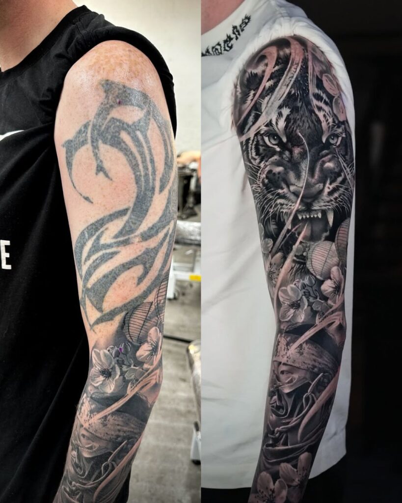 A black and grey sleeve tattoo coverup showing a tiger and samurai and the old tribal tattoo on the left of the image.