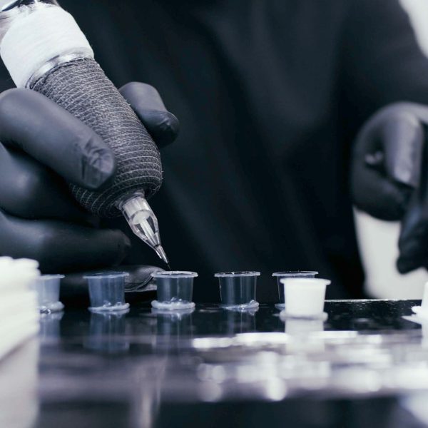 A tattoo artist dipping their needle into a pot of black ink.