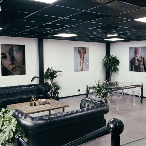 No Regrets Manchester. Image shows waiting area with white walls, photography on the walls and two black chesterfield sofas in the forgeround next to plants.