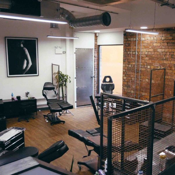A wide shot of the tattoo area at No Regrets Leeds. It shows a brick wall, black and white photography on a white wall and several tattoo chairs.