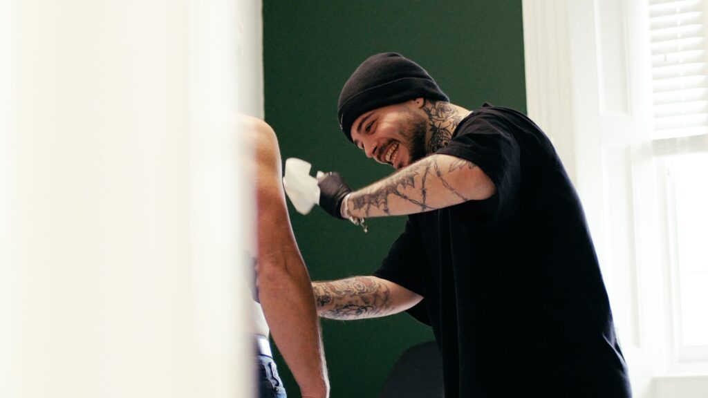 A No Regrets Miami tattoo artist smiling as he puts  stencil on a clients arm. 