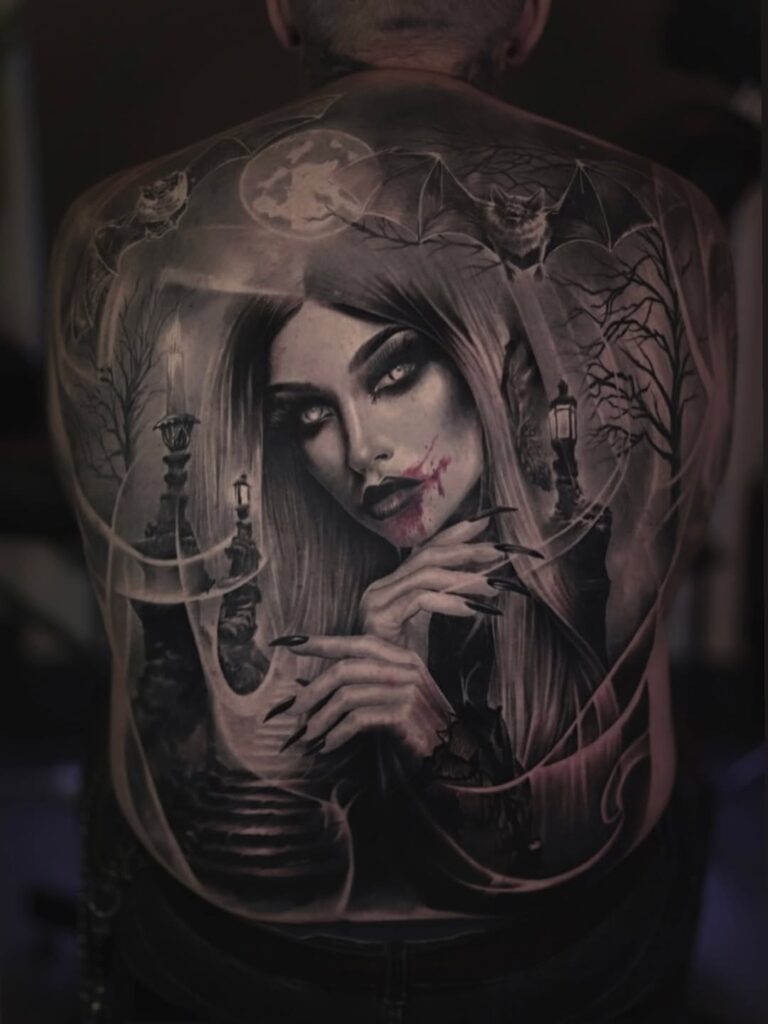 A black and gray backpiece of a female vampire and a spooky graveyard setting. 