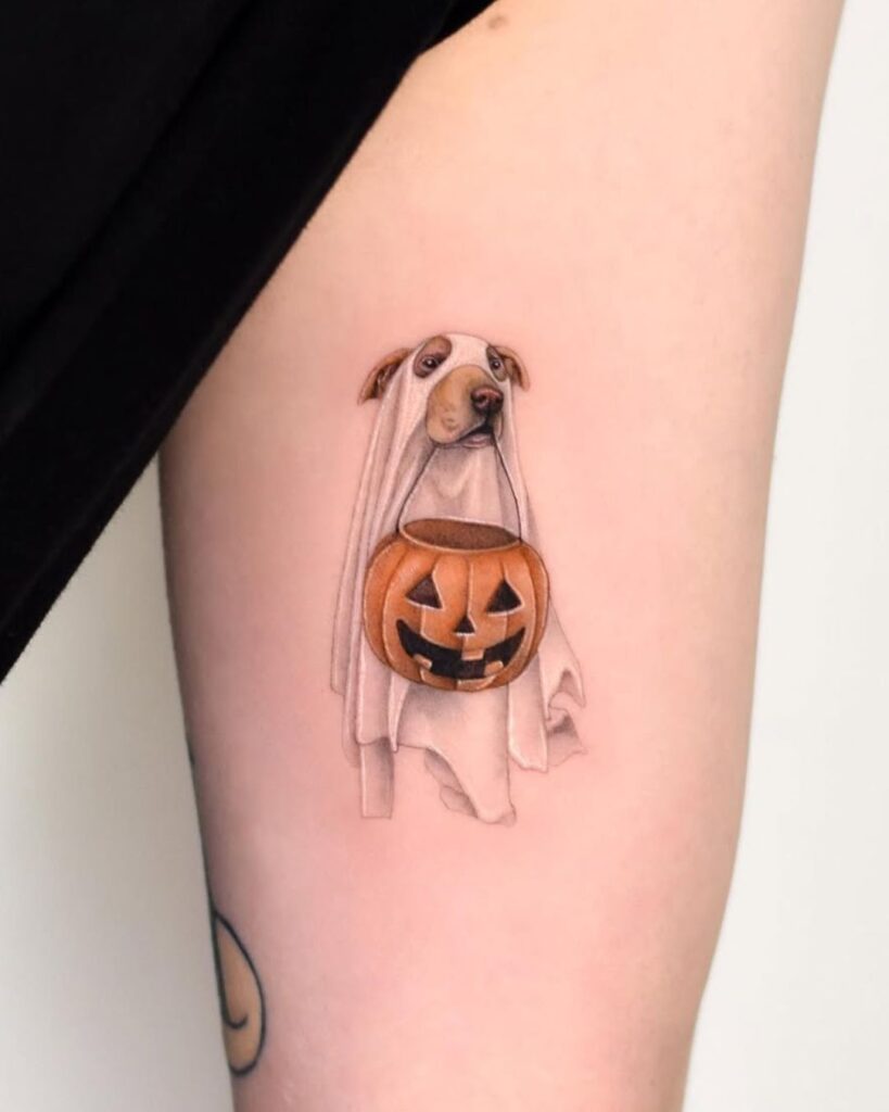 Cute halloween tattoos: A micro realism tattoo of a dog dressed up as a ghost holding a jack-o-lantern candy bucket in its mouth. 