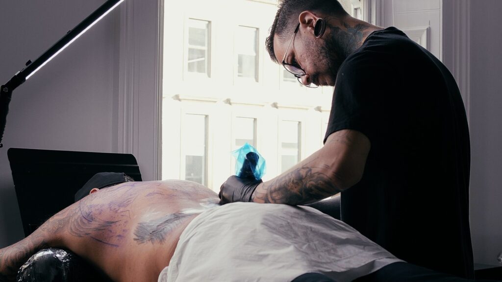 Jean Henrique stands over a man lying down as he tattoos his back at our Wynwood Tattoo studio 