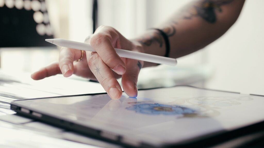 A close up of an artists hand on their iPad, drawing a tattoo design.