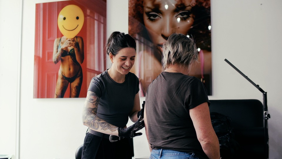 A female tattoo artist cleans a tattoo on the arm of a female tattoo client at No Regrets Glasgow