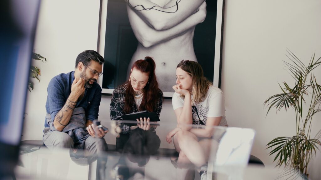 A man and two women sit on a bench at No Regrets Miami discussing tattoos during their consultation